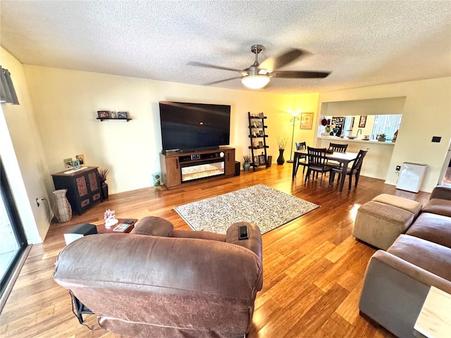 living area with ceiling fan, a textured ceiling, and wood finished floors