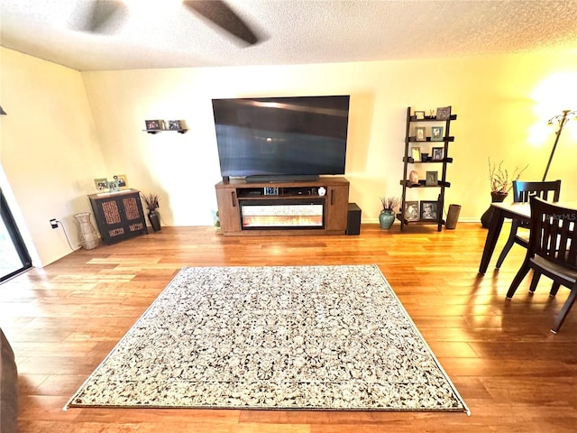 living area featuring a textured ceiling, a ceiling fan, and wood finished floors