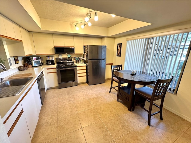 kitchen featuring black appliances, a tray ceiling, light countertops, and a sink