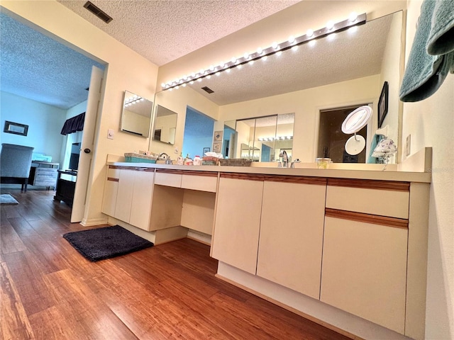 bathroom with double vanity, visible vents, a sink, a textured ceiling, and wood finished floors