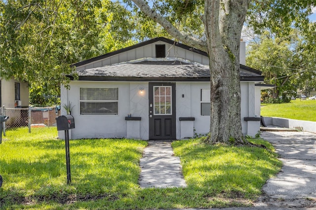 view of front of home with roof with shingles, a front yard, fence, and stucco siding