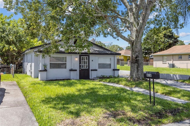 bungalow-style house featuring central air condition unit, fence, a front lawn, and stucco siding