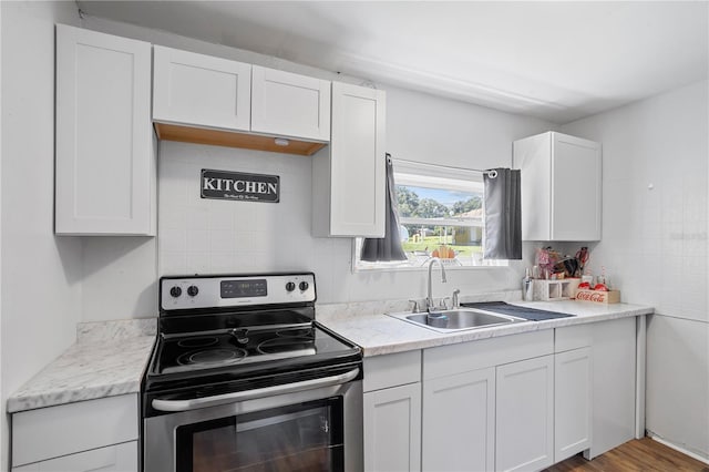 kitchen featuring stainless steel range with electric stovetop, white cabinetry, a sink, and backsplash