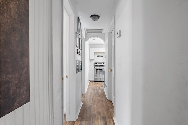 hall with baseboards, visible vents, arched walkways, and wood finished floors