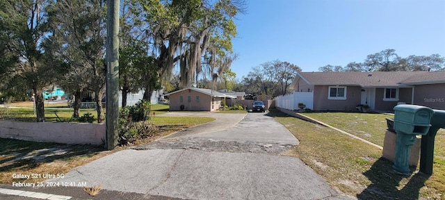 exterior space featuring concrete driveway, a front lawn, and fence