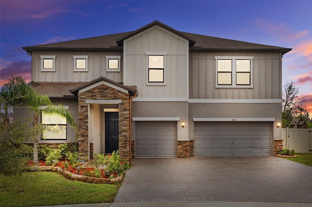 view of front facade with a garage, a shingled roof, stone siding, decorative driveway, and board and batten siding