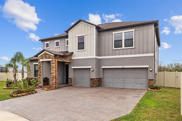 view of front facade with an attached garage, fence, stone siding, decorative driveway, and board and batten siding