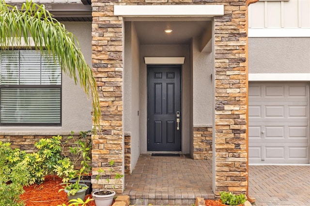 doorway to property featuring a garage, stone siding, and stucco siding