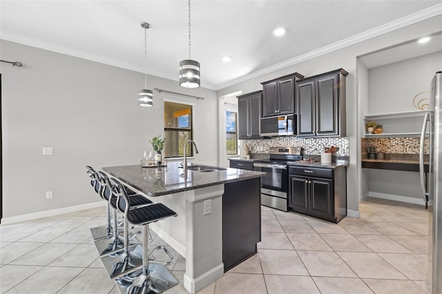 kitchen with dark stone counters, an island with sink, appliances with stainless steel finishes, a kitchen breakfast bar, and a sink