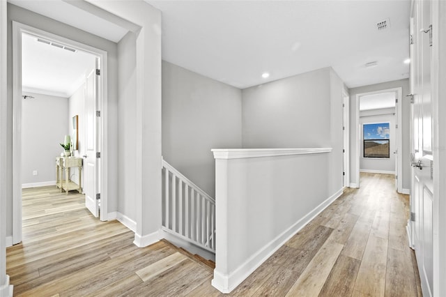 corridor featuring light wood-style floors, baseboards, visible vents, and an upstairs landing