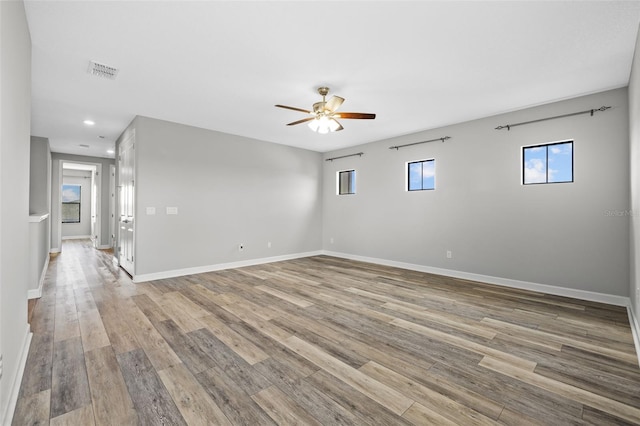 empty room with light wood-style flooring, a ceiling fan, visible vents, and baseboards