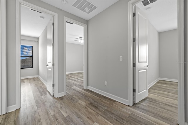 corridor featuring light wood-style flooring, visible vents, and baseboards