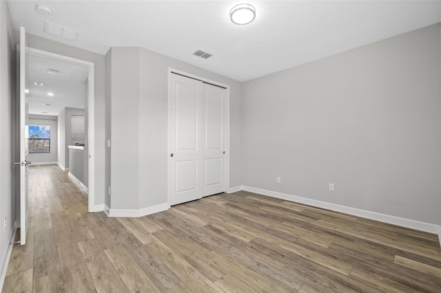 unfurnished bedroom featuring visible vents, a closet, baseboards, and wood finished floors