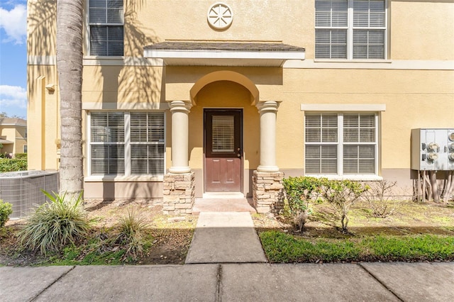 view of exterior entry with stone siding, central AC, and stucco siding