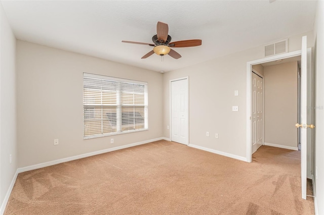 empty room with baseboards, visible vents, ceiling fan, and light colored carpet