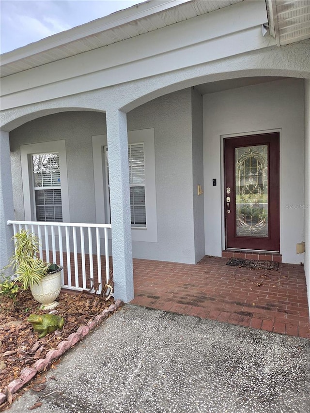 doorway to property with a porch and stucco siding