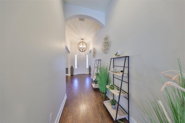 hallway featuring arched walkways, dark wood finished floors, visible vents, and baseboards