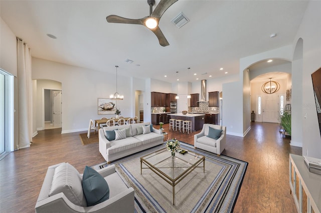 living area with arched walkways, dark wood-style flooring, visible vents, baseboards, and ceiling fan with notable chandelier