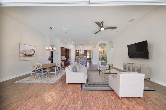 living room featuring baseboards, arched walkways, dark wood-type flooring, and ceiling fan with notable chandelier