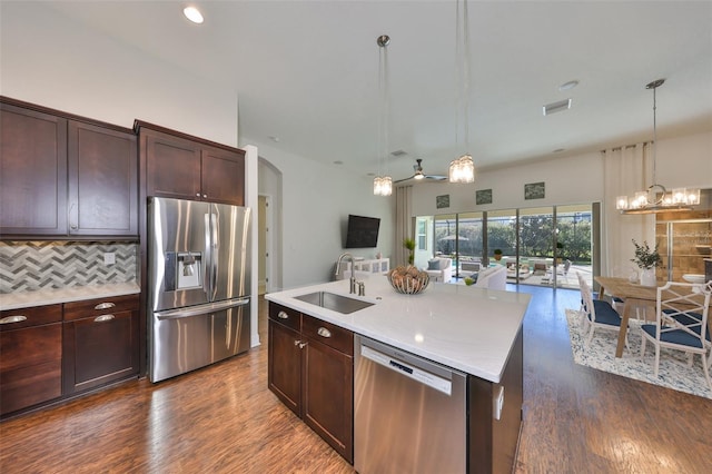 kitchen with stainless steel appliances, light countertops, open floor plan, a sink, and an island with sink