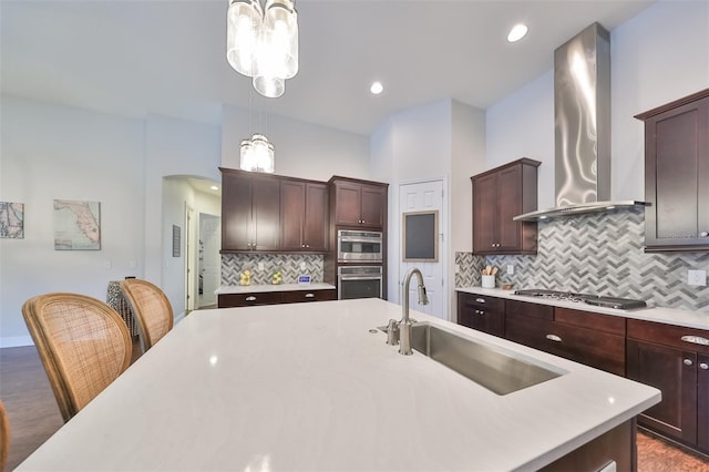 kitchen with appliances with stainless steel finishes, hanging light fixtures, light countertops, wall chimney range hood, and a sink