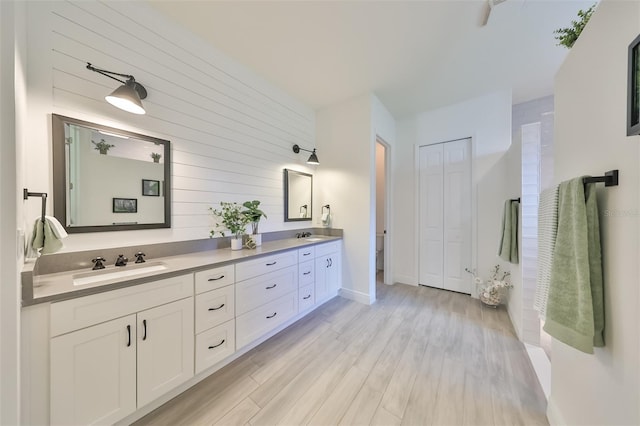 full bath with double vanity, wood finished floors, a closet, and a sink