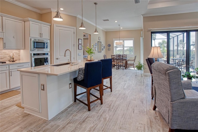 kitchen with a kitchen island with sink, a sink, white cabinetry, light countertops, and appliances with stainless steel finishes