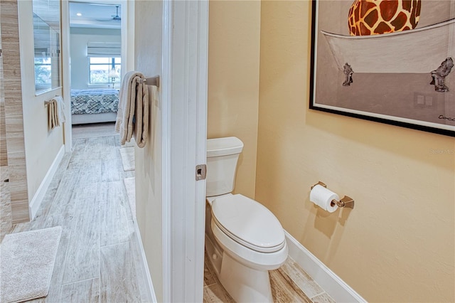 ensuite bathroom with toilet, connected bathroom, baseboards, and wood finished floors