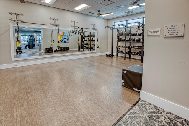 gym with ceiling fan, a drop ceiling, and baseboards