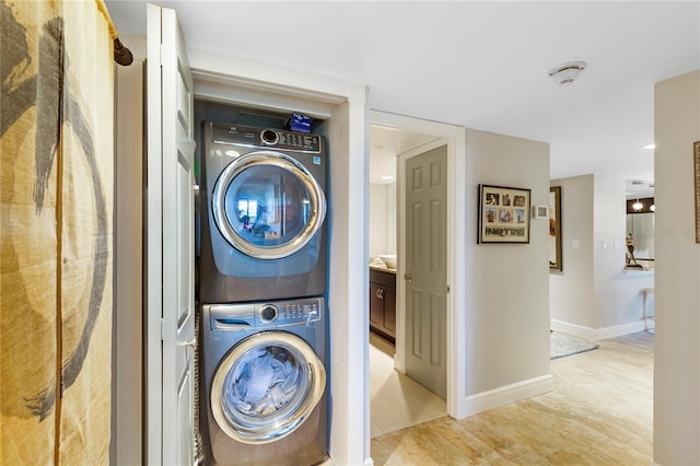 washroom with light wood-style floors, laundry area, baseboards, and stacked washer / drying machine