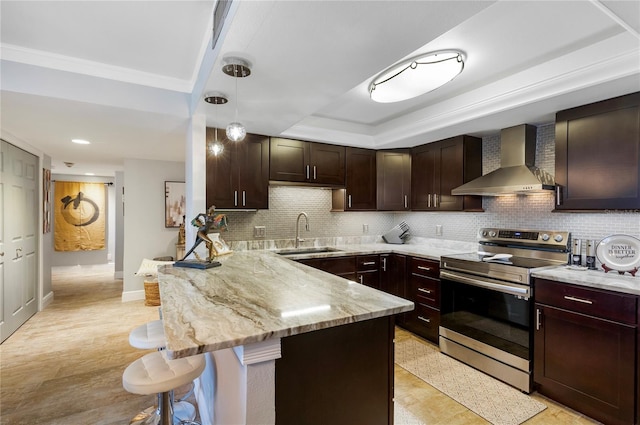 kitchen featuring wall chimney range hood, a peninsula, a tray ceiling, stainless steel range with electric stovetop, and a sink