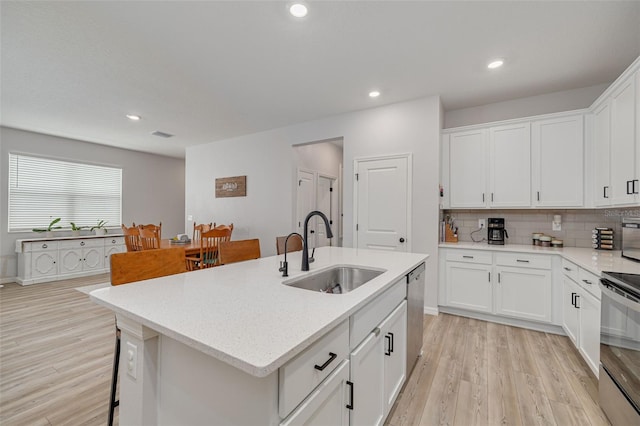 kitchen with light wood-style flooring, a sink, white cabinetry, dishwasher, and a center island with sink