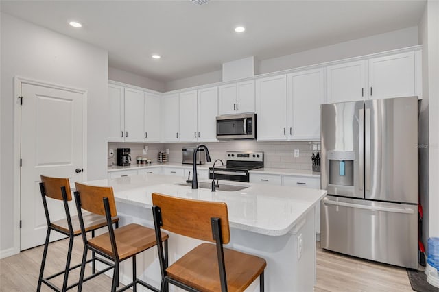 kitchen featuring white cabinets, an island with sink, light wood-style flooring, stainless steel appliances, and a kitchen bar