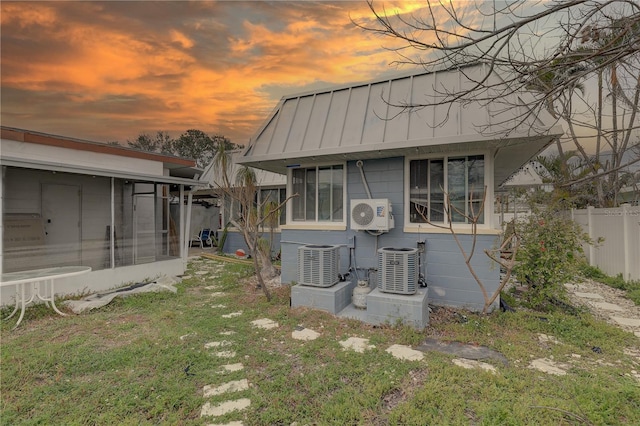 back of house at dusk with a lawn, central AC unit, a standing seam roof, metal roof, and fence