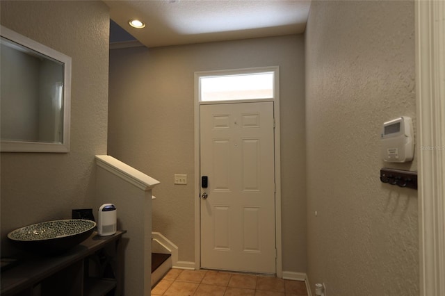 foyer entrance with light tile patterned flooring, a textured wall, and baseboards