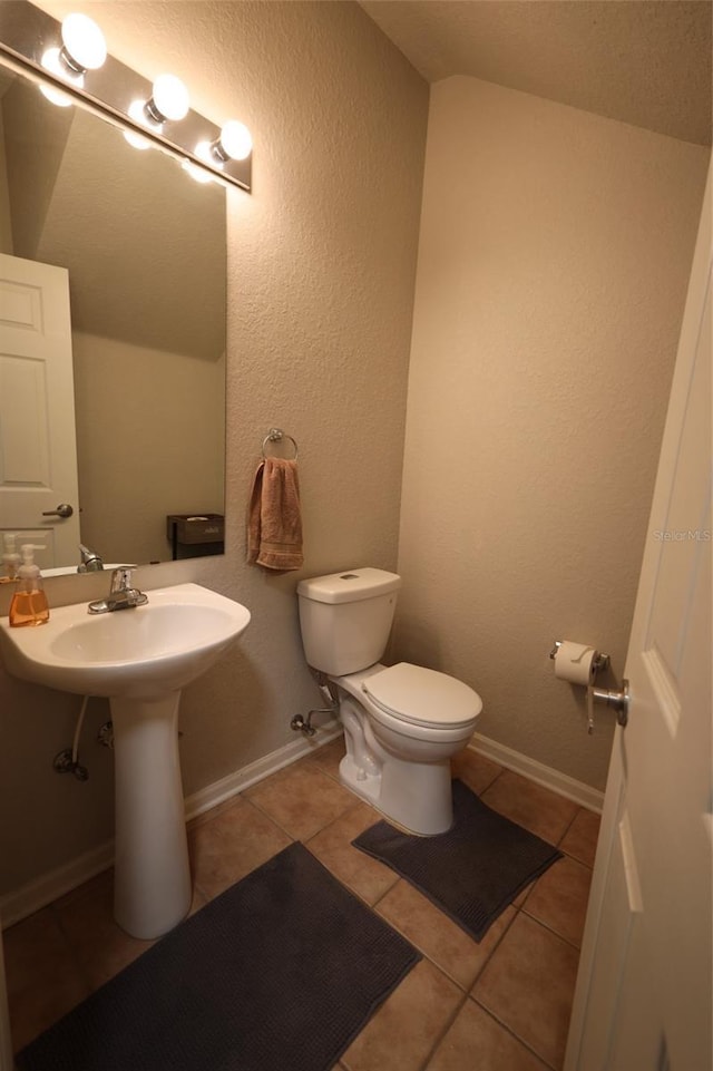 bathroom featuring baseboards, a textured wall, toilet, and tile patterned floors