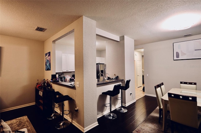 dining area featuring a textured ceiling, dark wood-style flooring, visible vents, and baseboards