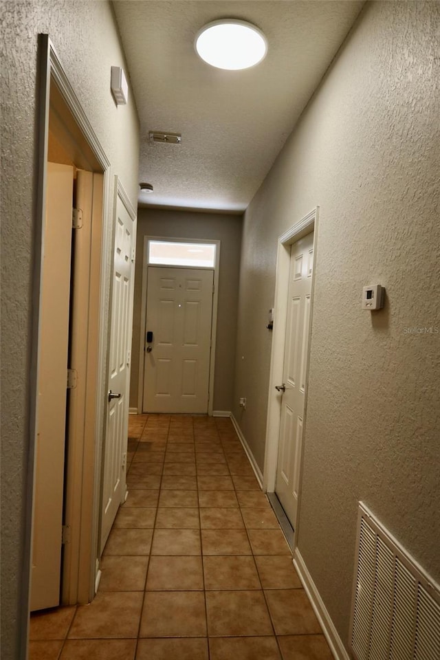 hallway featuring light tile patterned floors, a textured wall, a textured ceiling, and visible vents