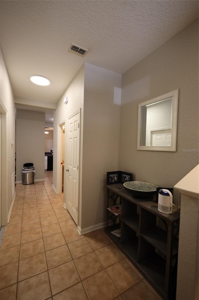 hall featuring visible vents, a textured ceiling, baseboards, and light tile patterned floors