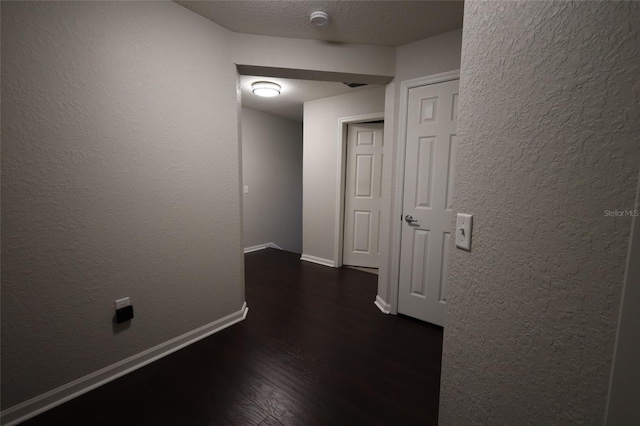 hallway featuring a textured ceiling, a textured wall, dark wood finished floors, and baseboards