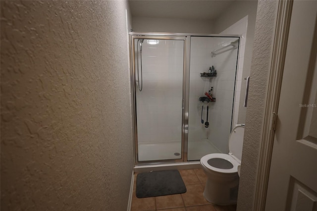 bathroom featuring toilet, a stall shower, tile patterned flooring, and a textured wall