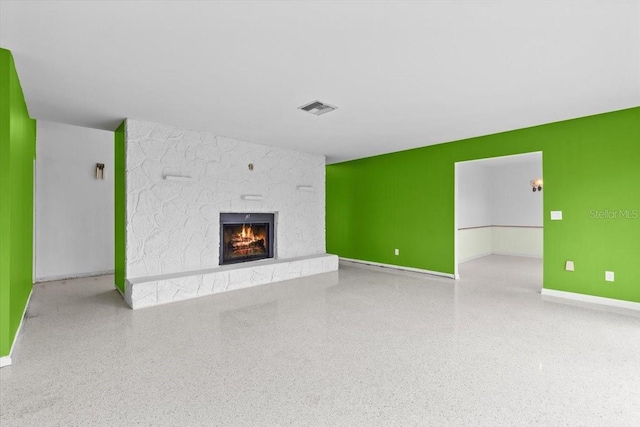 unfurnished living room featuring speckled floor, a fireplace, visible vents, and baseboards