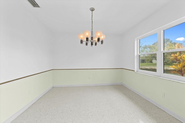 empty room with visible vents, baseboards, a notable chandelier, and speckled floor