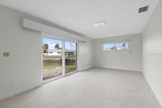 unfurnished room featuring a healthy amount of sunlight, visible vents, a textured ceiling, and baseboards