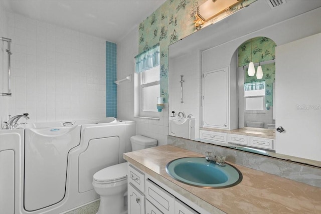 full bath featuring toilet, vanity, a washtub, and tile walls