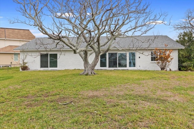 rear view of property with a yard, roof with shingles, and stucco siding