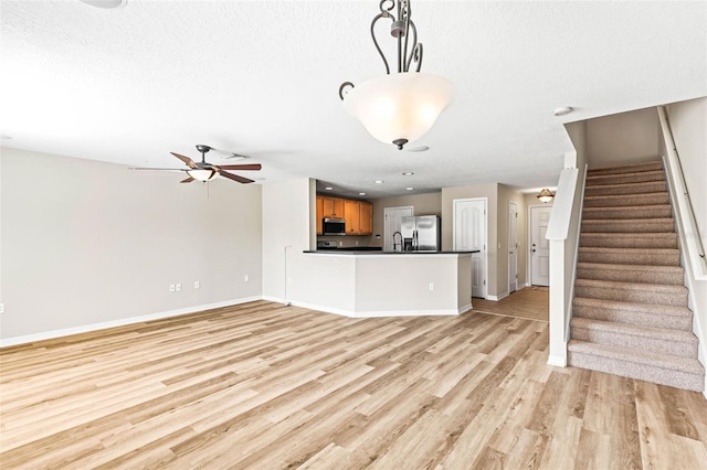 unfurnished living room featuring light wood finished floors, baseboards, stairway, and ceiling fan