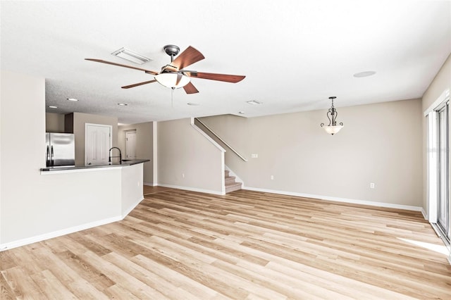 unfurnished living room featuring light wood-style floors, stairs, baseboards, and a sink