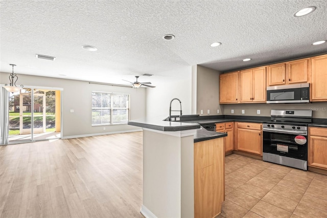 kitchen featuring stainless steel appliances, dark countertops, a sink, and a peninsula