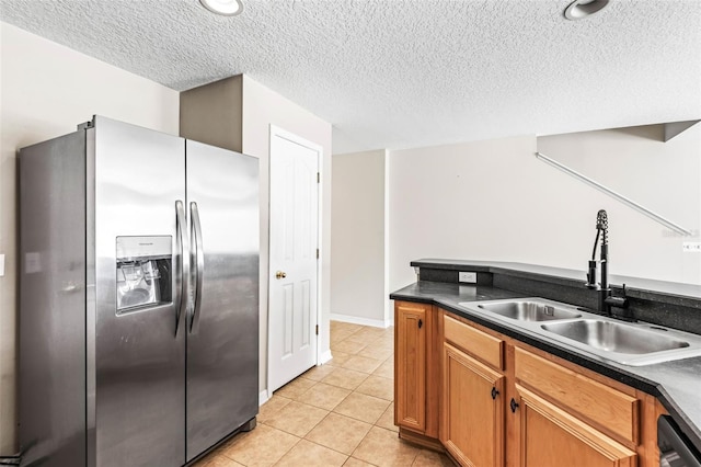 kitchen with light tile patterned floors, a sink, stainless steel refrigerator with ice dispenser, dishwasher, and dark countertops